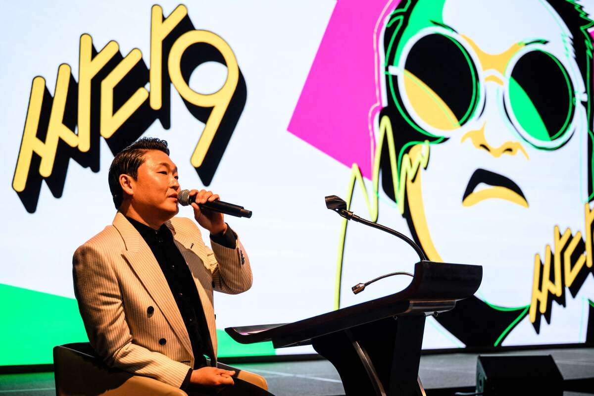 A man holding a microphone and wearing a suit jacket sits in front of a lectern