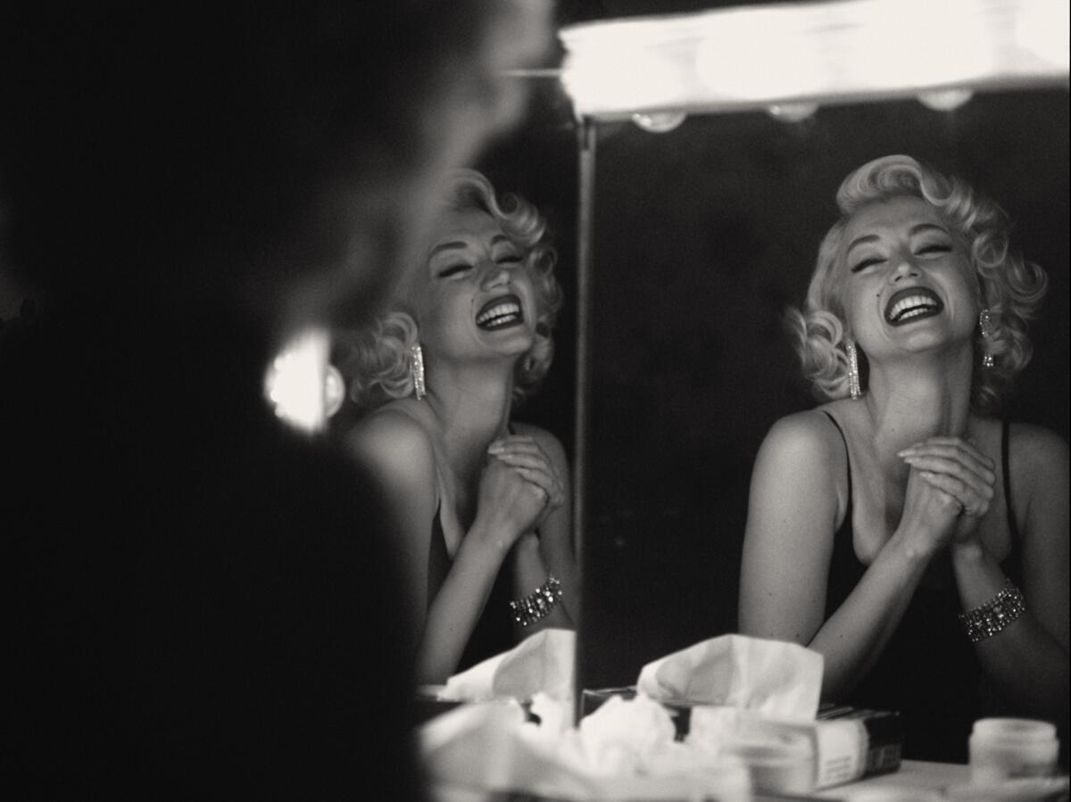 A black-and-white image of a blond woman smiling into a mirror.