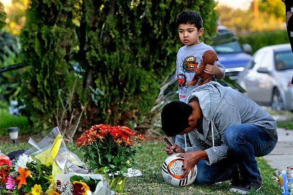 Rafael Guzman, with his 4-year-old brother, David, contributes to the memorial for his friend Francisco Rodriguez Jr., 17, who was shot to death in his frontyard Wednesday. Police don't have a motive or suspects yet.