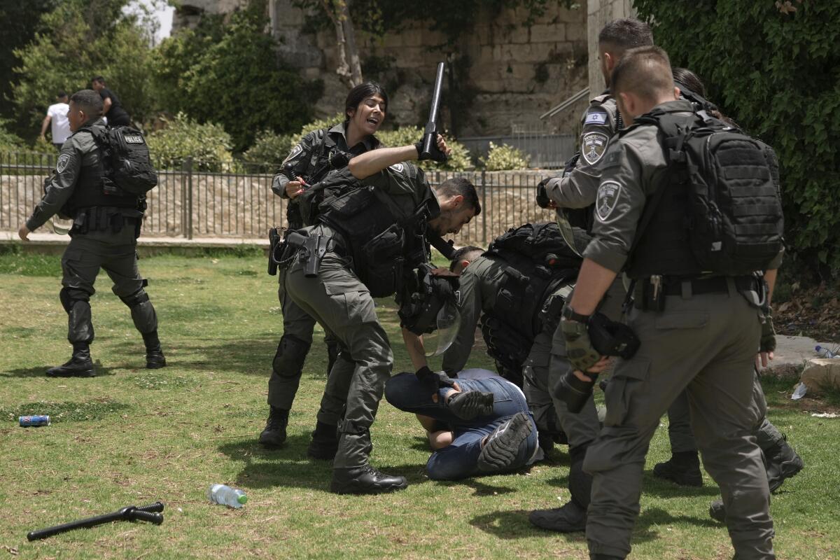 Members of Israeli security forces detain a Palestinian protester and one raises a baton over them.