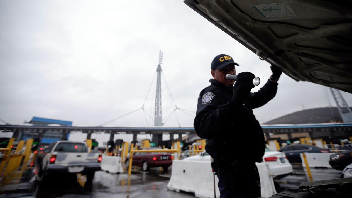 A U.S. Customs and Border Protection officer checks under the hood of a car as it waits to enter the U.S. from Tijuana, Mexico.