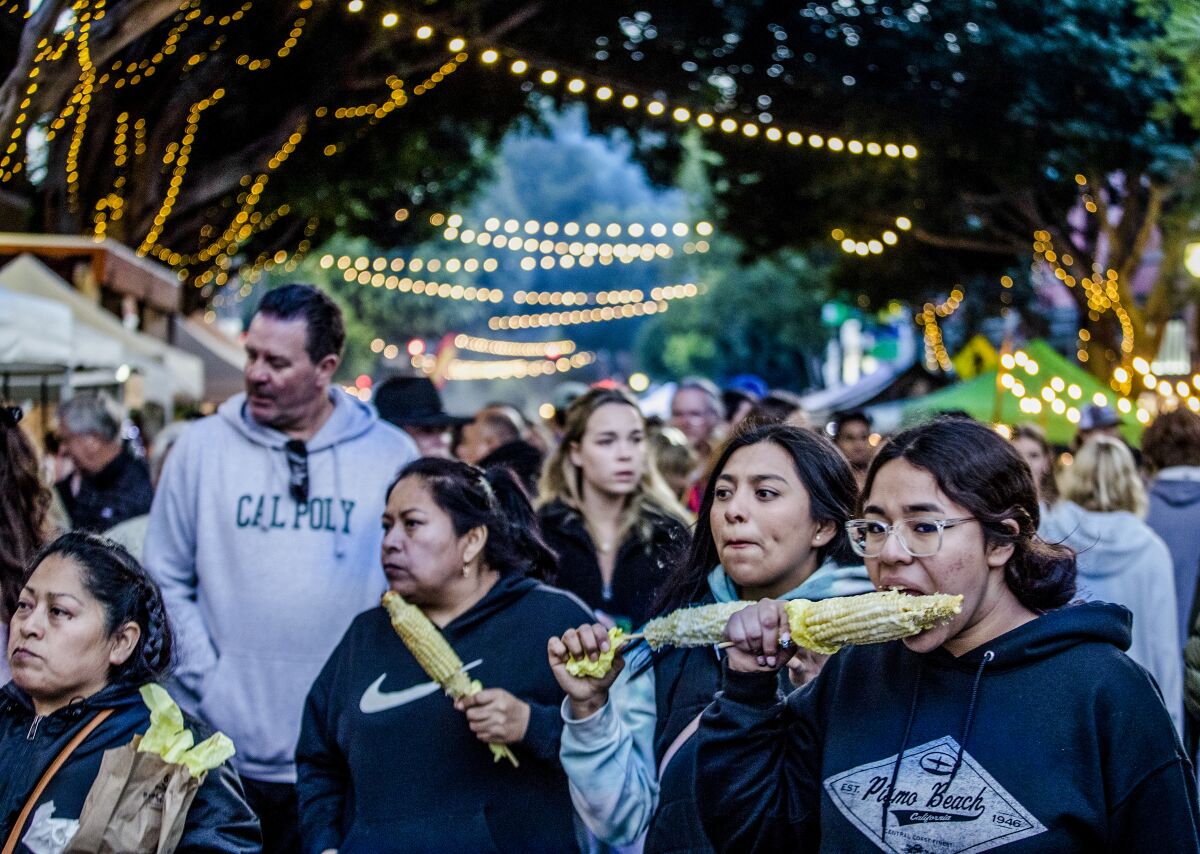 People eating corn on the cob at an outdoor market.