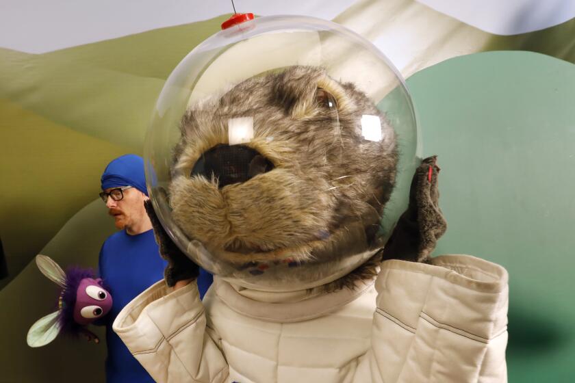 LOS ANGELES, CALIFORNIA-SEPT. 5, 2019-Gwen Hollander plays Astron-otter, the full-size otter dressed in a white astronaut suit. At left is Christian Anderson, (in the blue suit) who plays Sy the Wide-Eyed Fly. They prepare to shoot on the final day of filming. Gwen tries to get a grip on her large helmet during the final day of shooting. Welcome to the behind-the-scenes frenzy of "Mr. Pickles' Puppet Time," the children's show within the very adult show "Kidding," the comedy-drama featuring Jim Carrey as a Mister Rogers-esque TV host struggling to maintain a grip on his sanity after a horrific family tragedy. Photographs taken on (Carolyn Cole/Los Angeles Times)