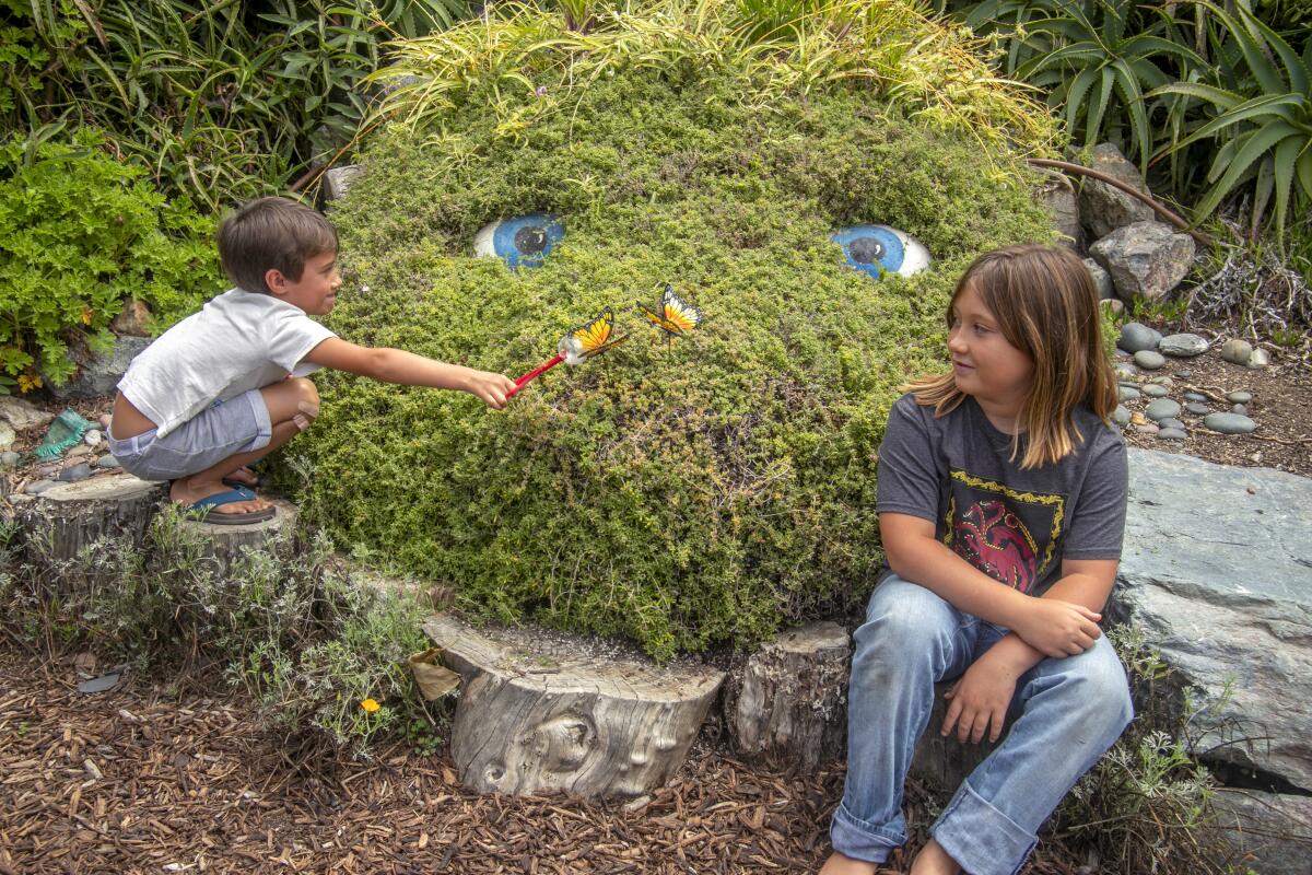Two children are shown in front of a topiary with large eyes.