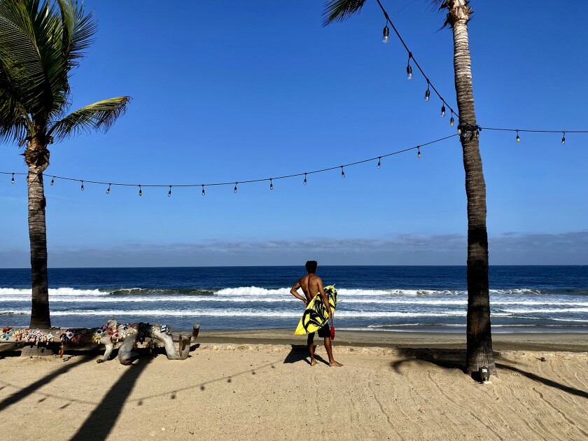 A surfer surveys the waves along a two-mile stretch of sand beach in front of a luxury retreat in Mexico.