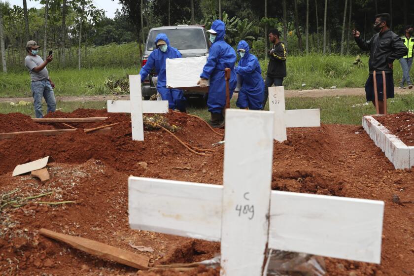 Workers in protective suits carry a coffin containing the body of a COVID-19 victim to a grave for a burial at Cipenjo cemetery in Bogor, West Java, Indonesia, Wednesday, July 14, 2021. The world's fourth most populous country has been hit hard by an explosion of COVID-19 cases that have strained hospitals on the main island of Java.(AP Photo/Achmad Ibrahim)