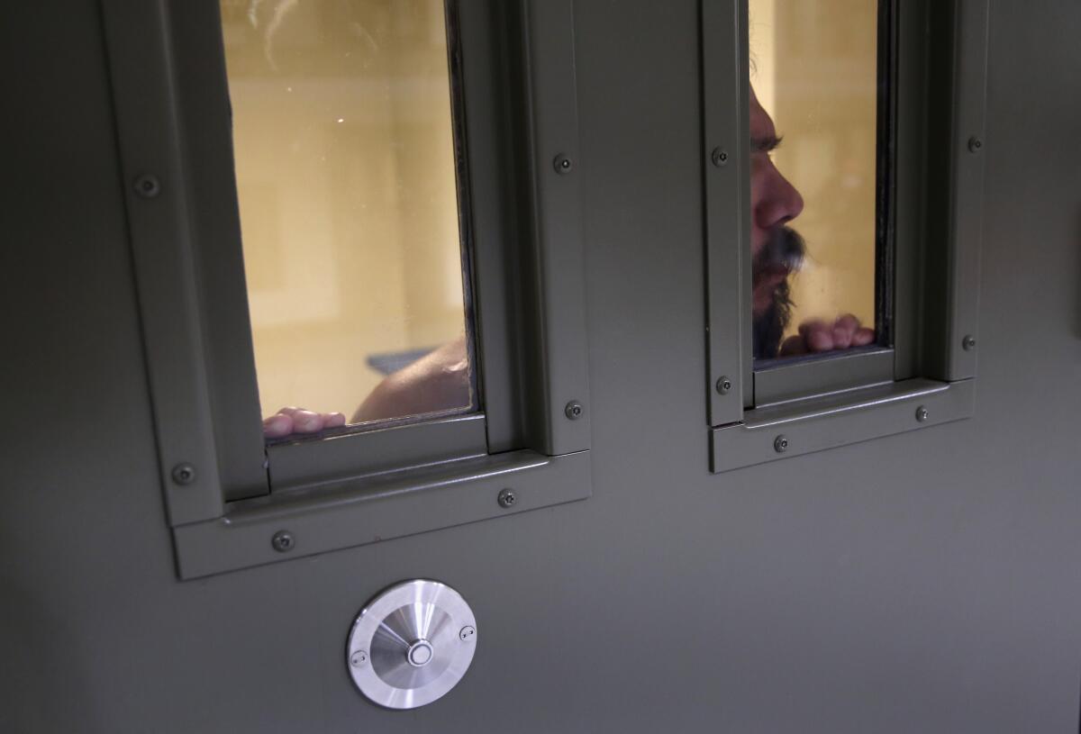 An immigrant detainee looks through a small window on the door of his cell.