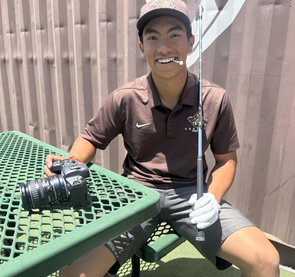 Grant Leary of Crespi High poses for a photo with a golf club and a camera.