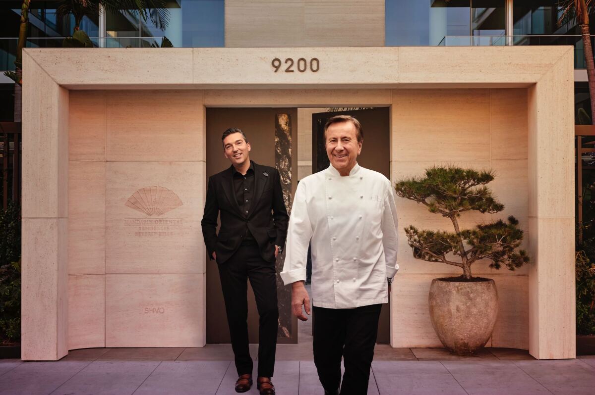 A man in a white chef's coat and a man in all black walk out of a building.