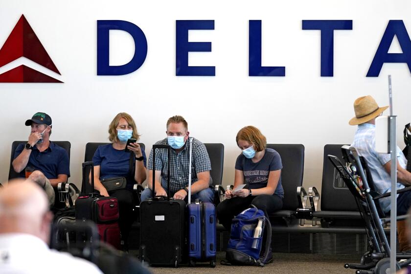 FILE - People sit under Delta sign at Salt Lake City International Airport on July 1, 2021, in Salt Lake City. Delta Air Lines won't force employees to get vaccinated, but it's going to make unvaccinated workers pay a $200 monthly charge. Delta said Wednesday, Aug. 25, 2021 that it will also require weekly testing for unvaccinated employees starting next month, although the airline says it'll pick up the cost of that testing. (AP Photo/Rick Bowmer, file)