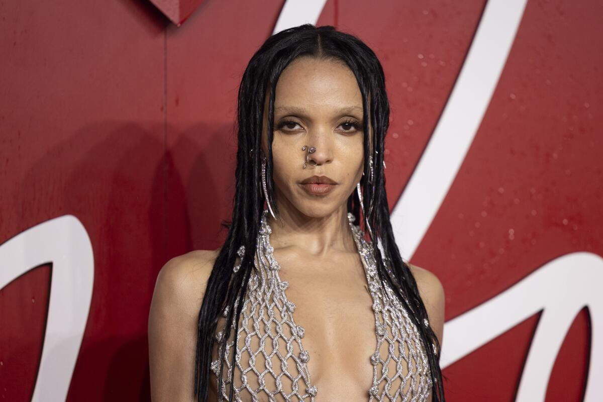 FKA Twigs wears a blush-colored crocheted top with nose jewelry and smoky eye makeup. 