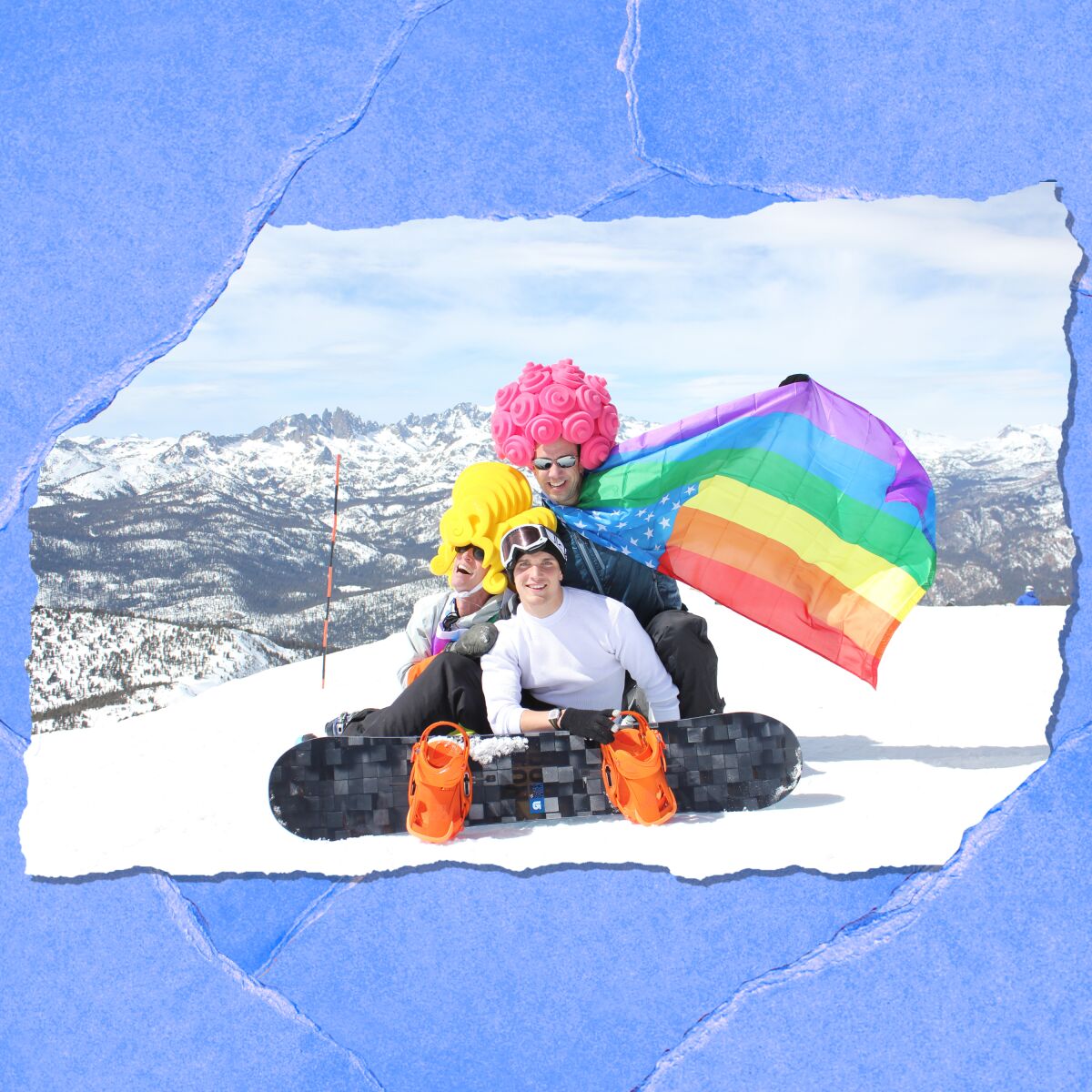 People in brightly colored wigs pose atop a snowy mountain. One holds out a rainbow flag.