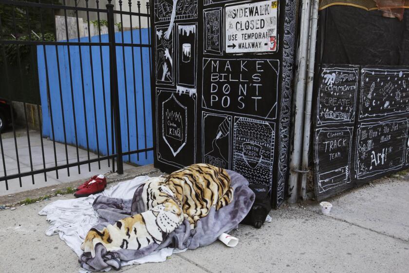 A homeless person sleeps under a blanket on a New York sidewalk.