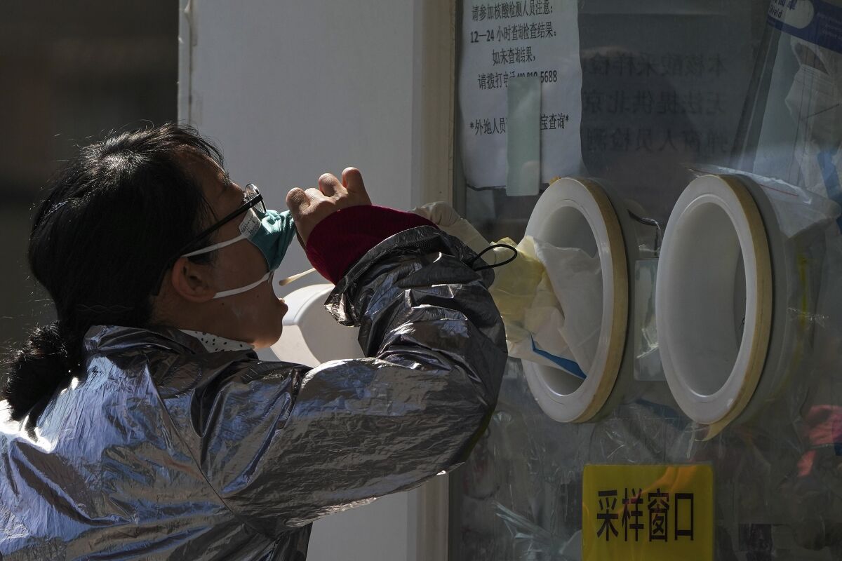 A woman pulls her face mask to get her routine COVID-19 throat swab at a coronavirus testing site in Beijing, Thursday, Oct. 6, 2022. Sprawling Xinjiang is the latest Chinese region to be hit with sweeping COVID-19 travel restrictions, as China further ratchets up control measures ahead of a key Communist Party congress later this month. (AP Photo/Andy Wong)