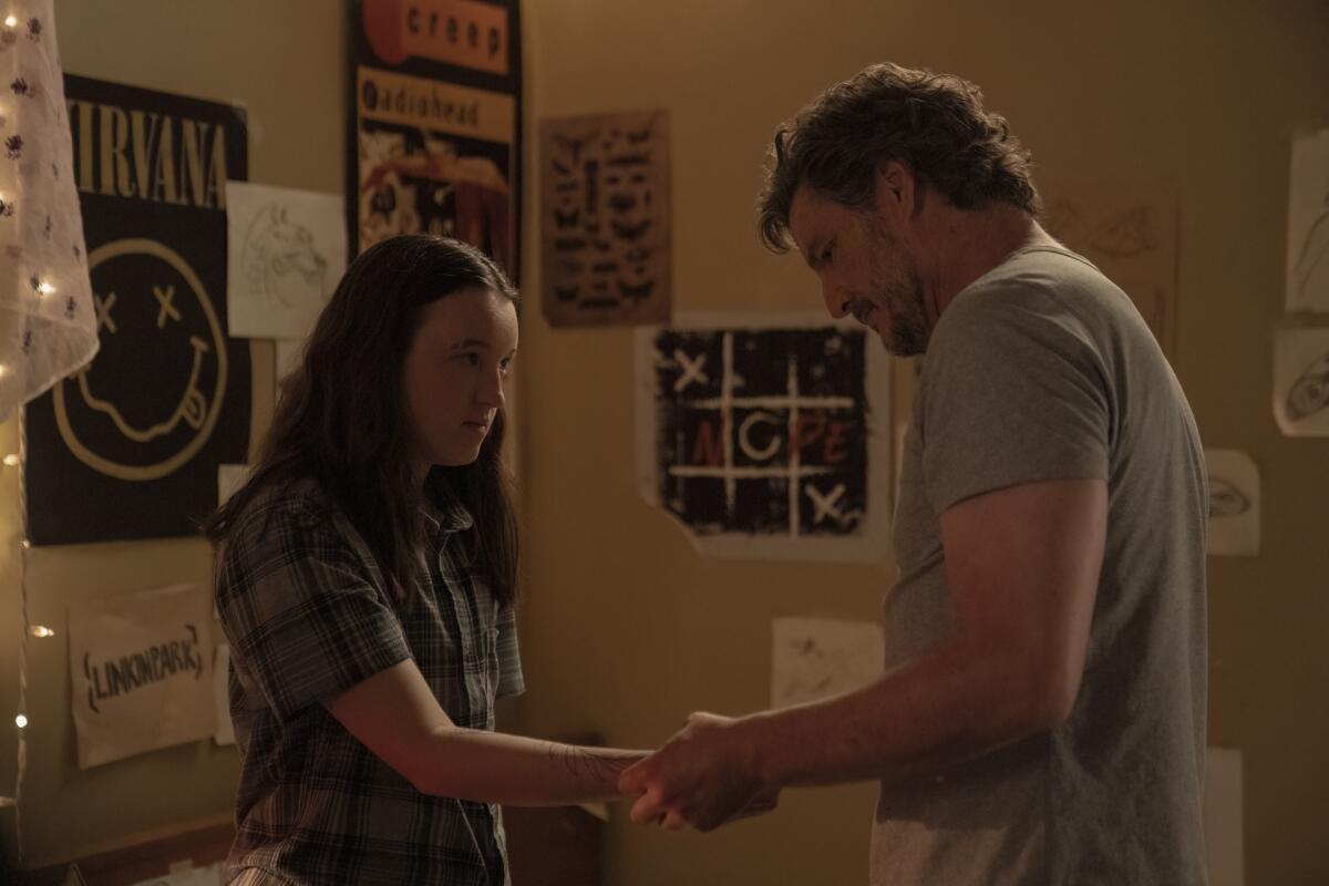 A teenage girl in a short-sleeve plaid shirt holds out her arm as a man looks down at it.