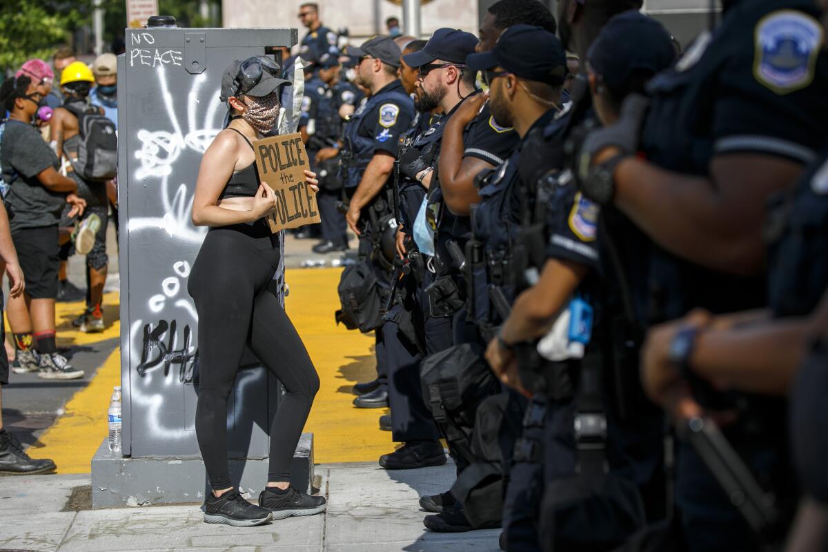 A woman holds up a sign saying "police the police" as she confronts a police line