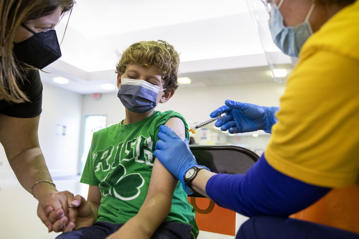 A child in a mask gets a shot in the upper arm.