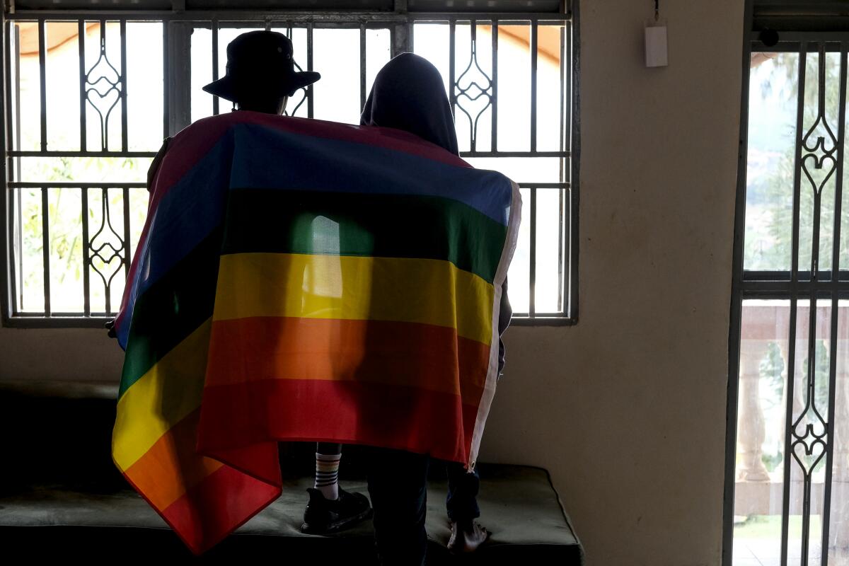 Gay Ugandan couple in shadow, draped in rainbow flag