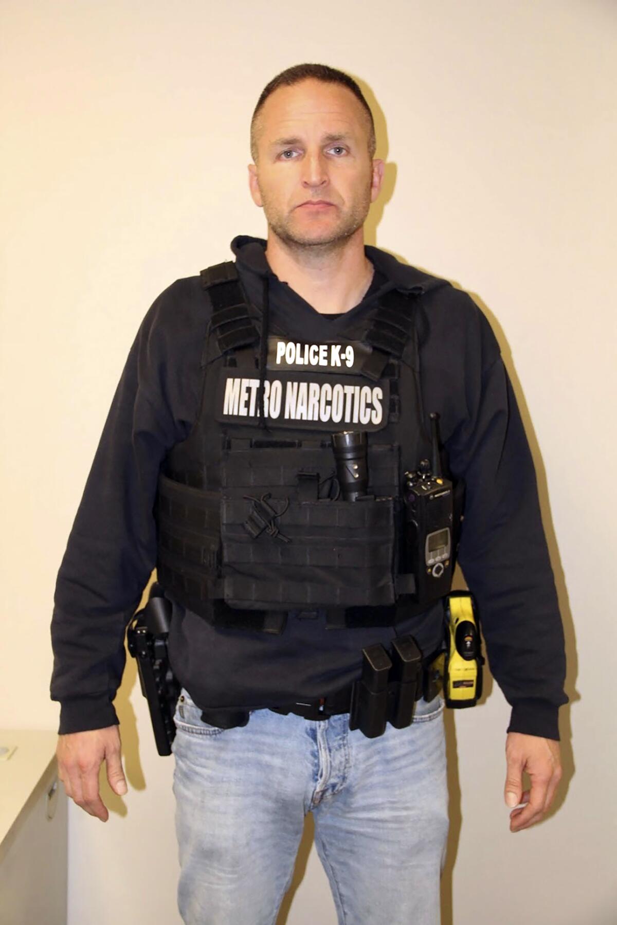 A man in a dark shirt and vest bearing the words "Police K-9 Metro Narcotics"