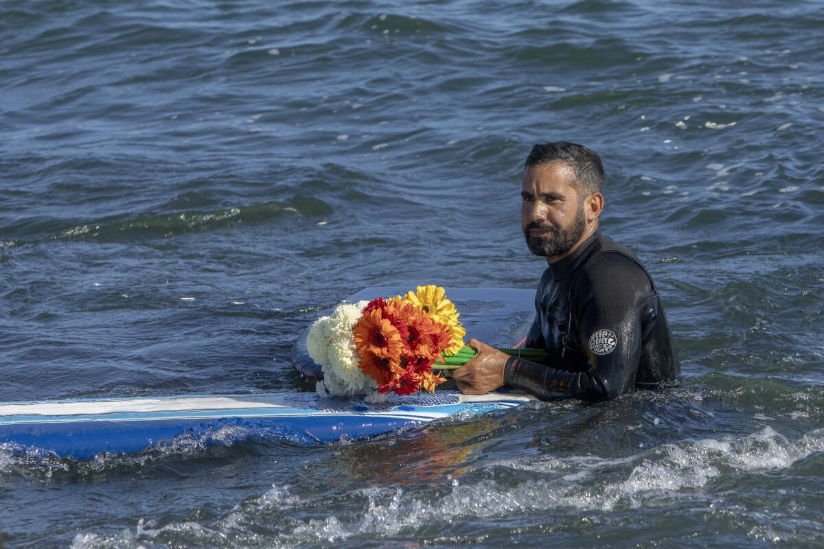A man holds flowers during a tribute to 3 missing surfers in Ensenada, Mexico.