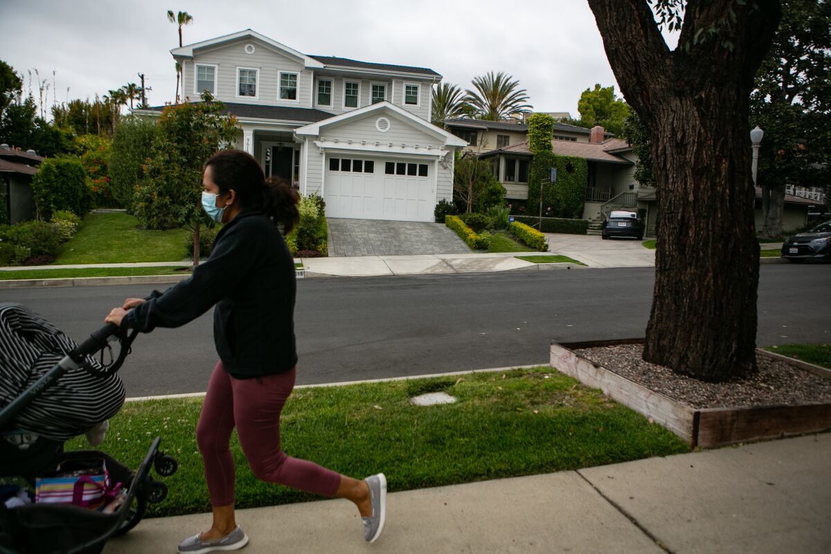 A woman walks and pushes a stroller in front of homes on a high-end residential street