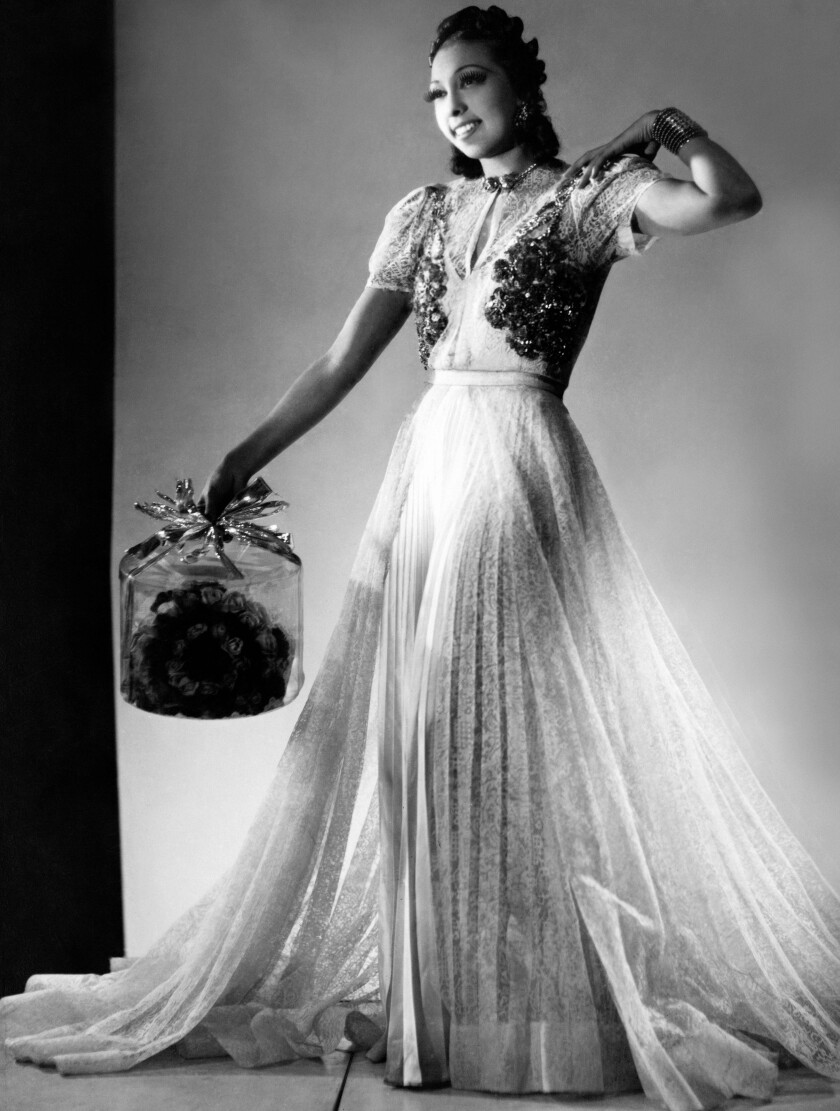 Josephine Baker poses in a glamorous dress holding a transparent hat box.