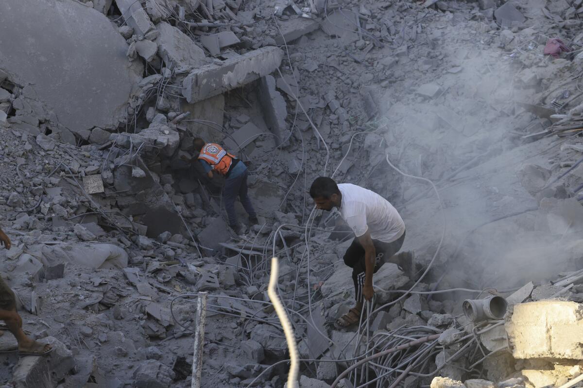 Palestinians search through a pit of dust-covered rubble.