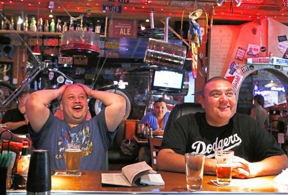 Dodgers fans Jose Zuniga, left, and Gabriel Aguilar react at Barney¿s Beanery in Burbank as they watch the team play the Philadelphia Phillies. Fans have poured into dining and drinking spots that show games.