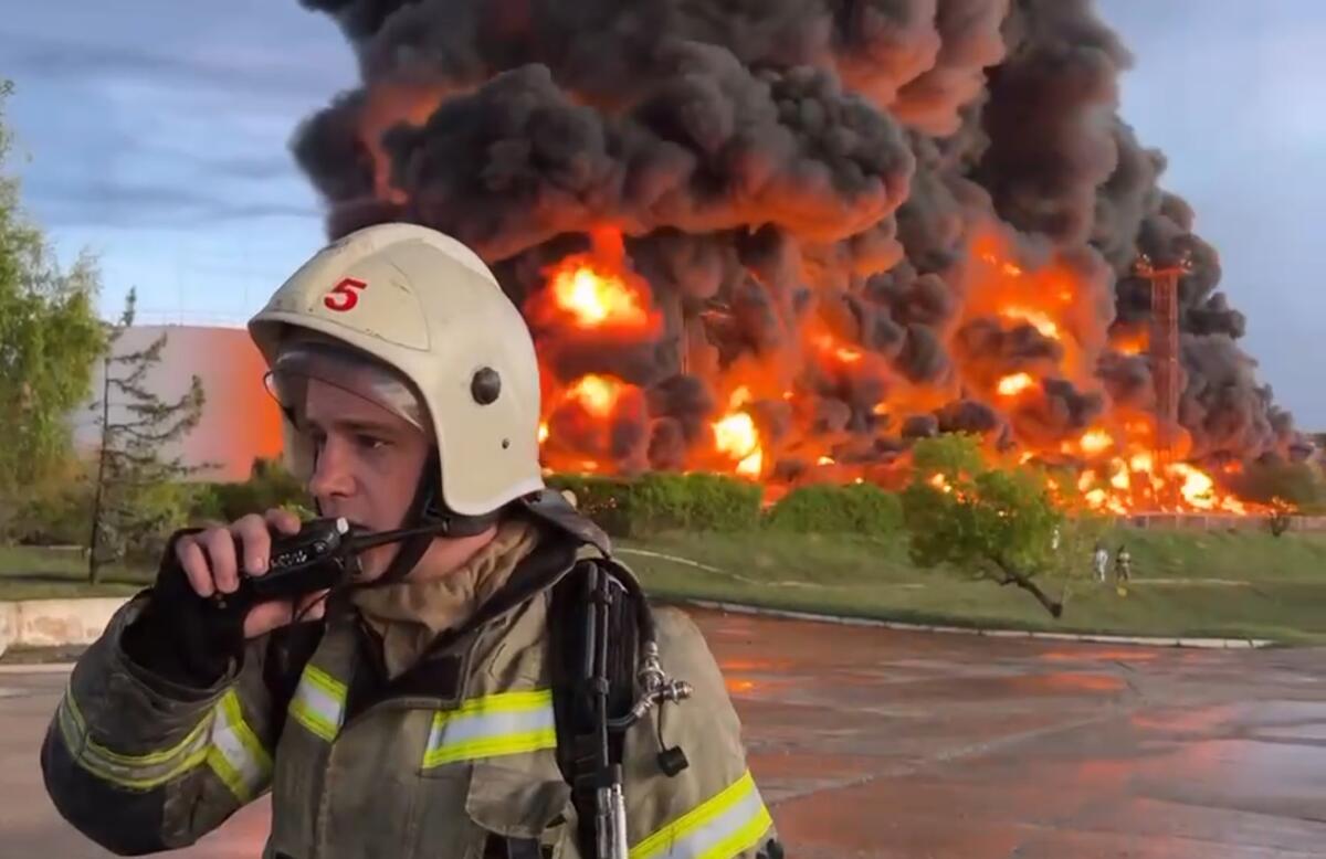 A firefighter stands in front of a plume of smoke and flames