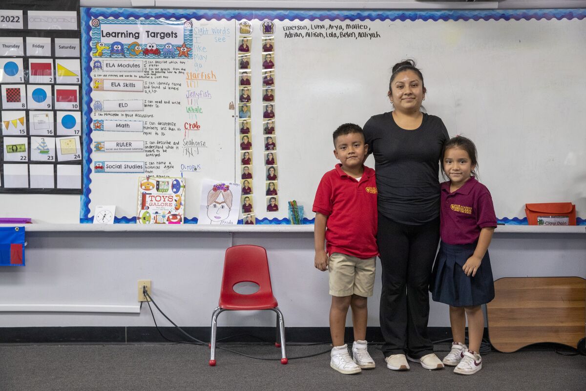 A woman and her two children stand in front of a whiteboard in a classroom