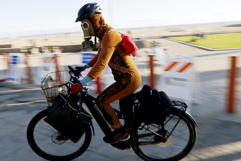 SANTA MONICA, CALIF. - APR. 17, 2020. Daniel Rogerson wears a vintage military gas mask while riding a bike along the beach path in Santa Monica, which is closed to enforce social distancing because of the coronavirus pandemic. (Luis Sinco/Los Angeles Times)