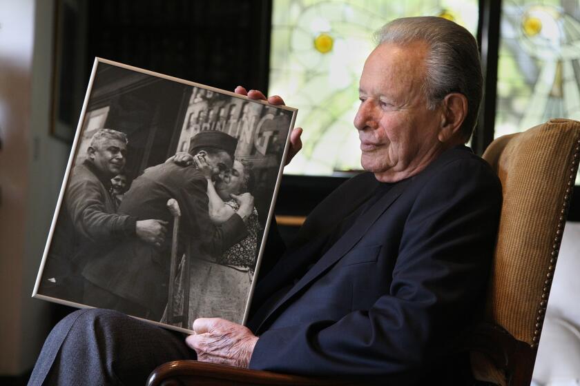 At his Beverly Hills home, film producer Mace Neufeld holds his 1944 photograph of a wounded Pvt. Sam Macchia being welcomed home from World War II by his parents in New York City. Neufeld was a 16-year-old high school senior when he snapped the photo, which made the short list for the 1945 Pulitzer Prize.