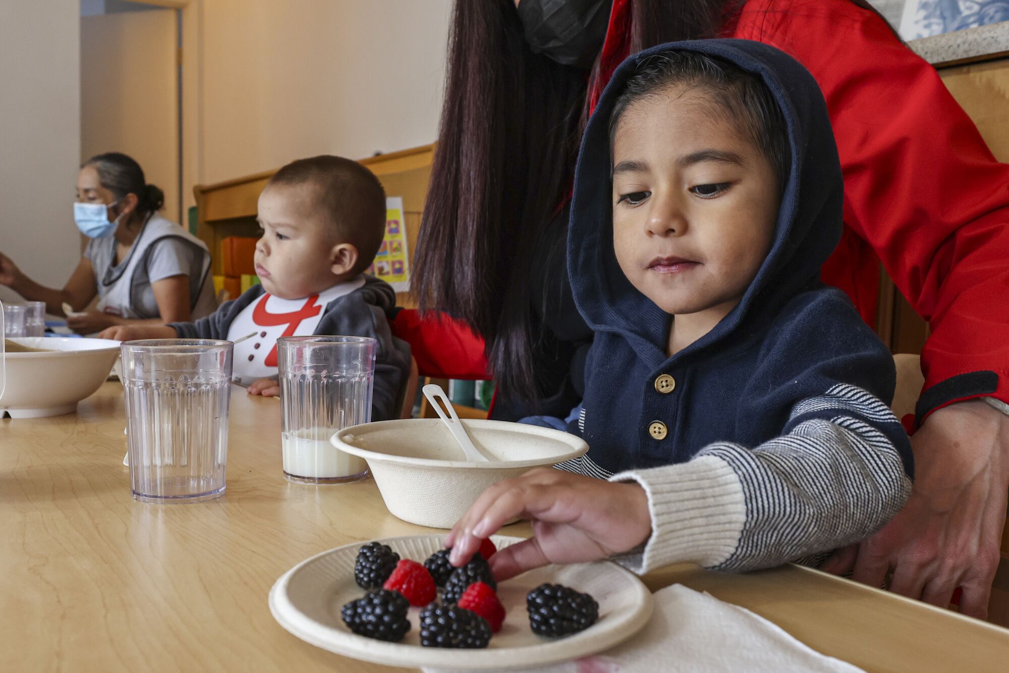 Adriel, 3, eats some berries with the other children whom child care provider Miren Algorri, standing, serves at her home.