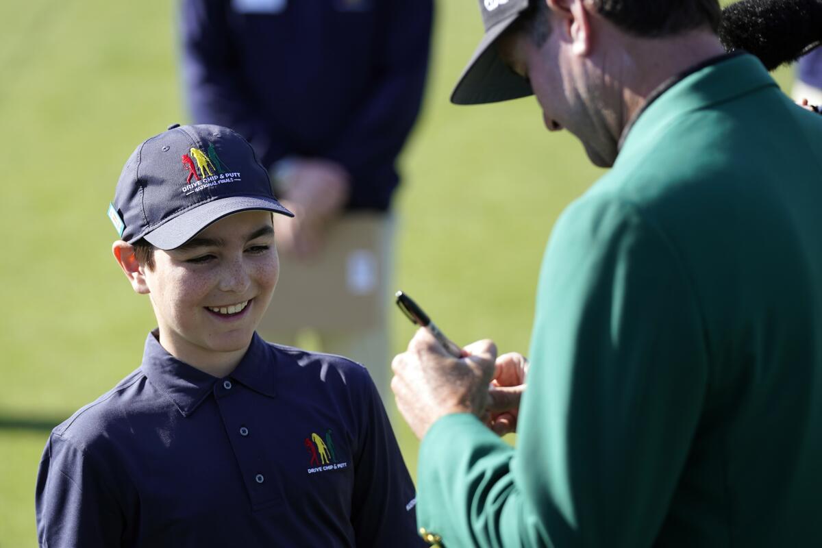 Lucas Bernstein, left, waits as Masters Champion Bubba Watson signs a golf ball for him during the Drive Chip & Putt National Finals at Augusta National Golf Club, Sunday, April 4, 2021, in Augusta, Ga. (AP Photo/David J. Phillip)