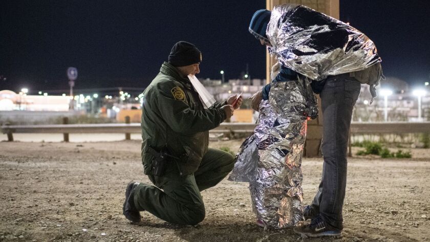 Border Patrol Agent Ramiro Cordero puts arm bands on Mairon Argueta and his daughter Elsi Argueta, 4, of Honduras, while they are wrapped in mylar blankets in El Paso, Texas, on Feb. 22.