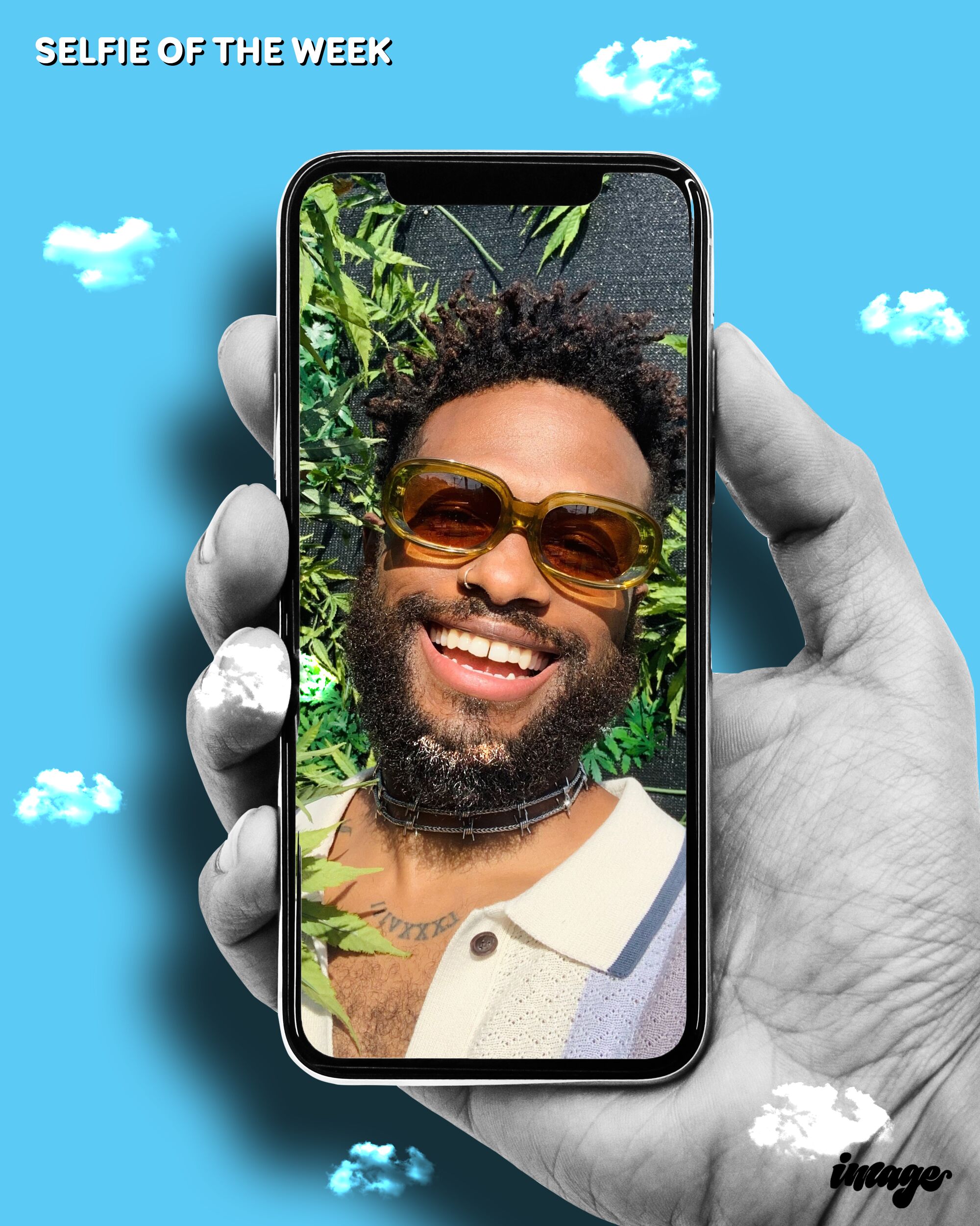 A hand holds a cellphone displaying a selfie of a smiling, bearded Black man in sunglasses.