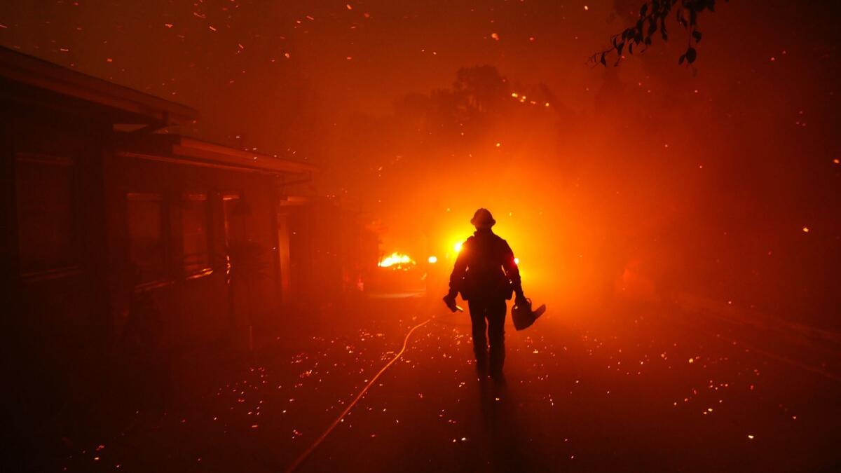 A firefighter walks towards his engine after trying to prevent the Woolsey fire from overtaking structures in Malibu Friday. No public schools in Ventura County were directly hit, but a Jewish school suffered significant damage.