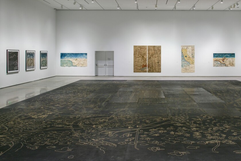Vista de galería de pinturas de mapas y una pieza cortada con láser colocada en el suelo.