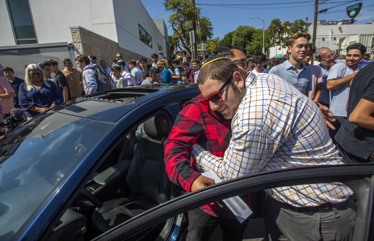 A student hugs his teacher next to a car. 