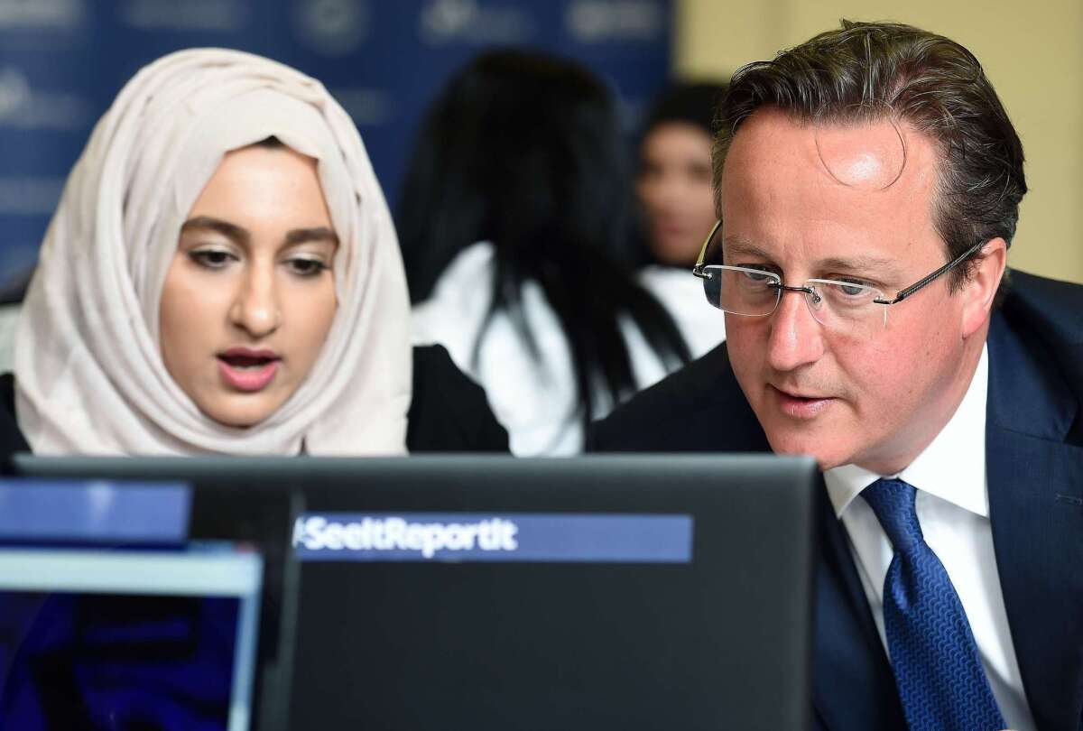 British Prime Minister David Cameron, visiting Ninestiles Academy in Birmingham on Monday, looks at a computer as he speaks with Zahra Qadir during a workshop about ways to report suspicious online activity.