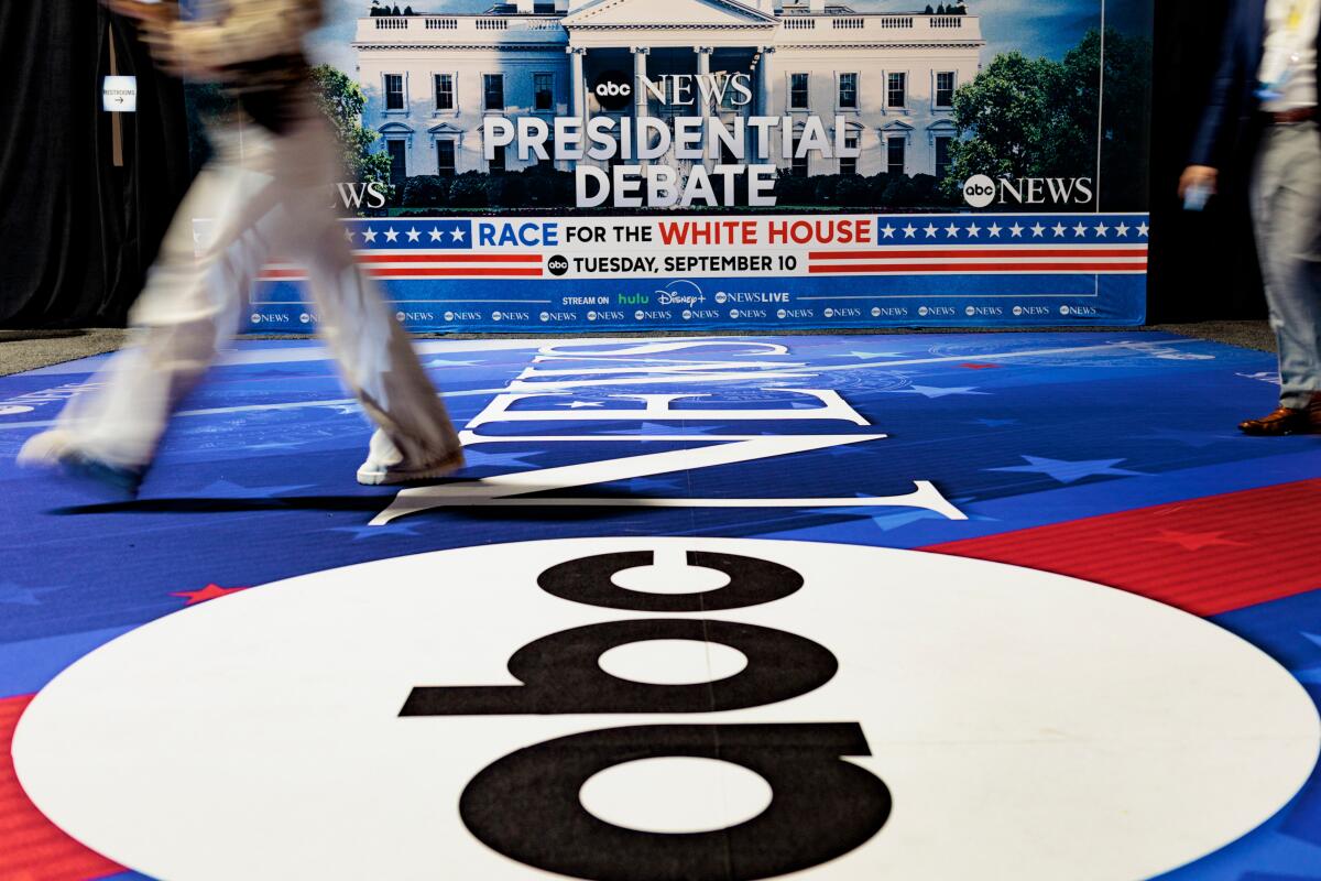 People cross a floor with the ABC News logo next to a "Presidential Debate" backdrop.