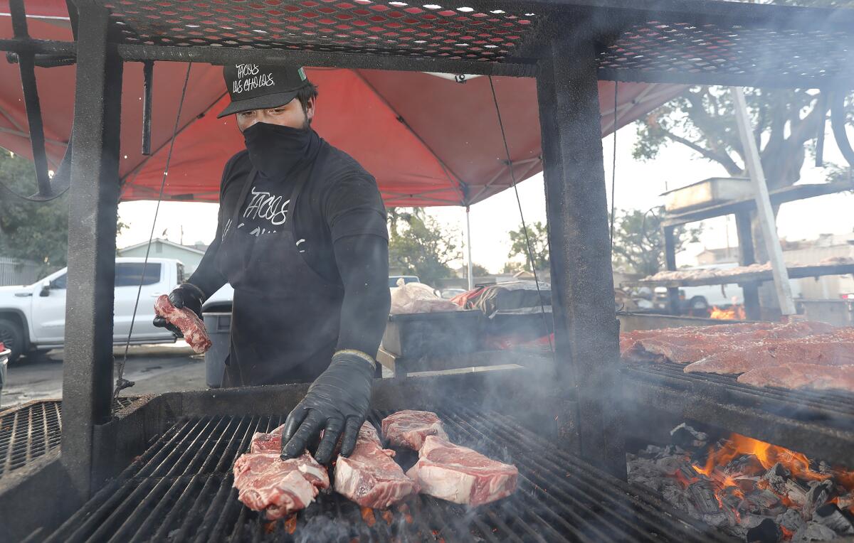 Rib-eye steaks cook over a mesquite wood fire at Tacos Los Cholos in Anaheim on Tuesday.