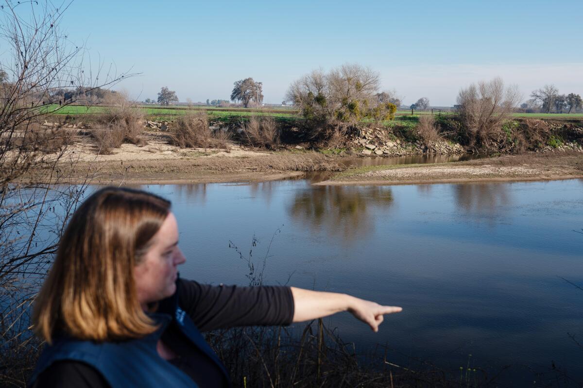 A woman points toward a body of water. 