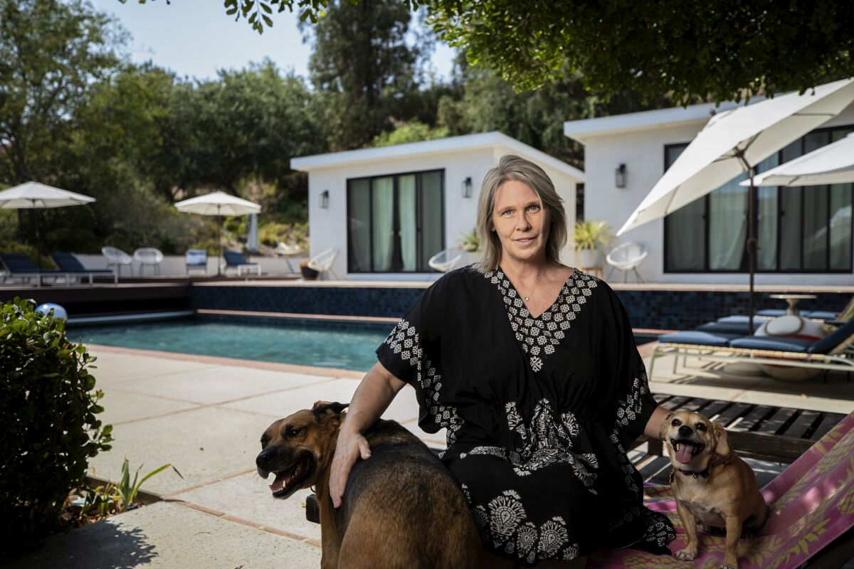 A woman sits outside with her dogs beside a backyard pool