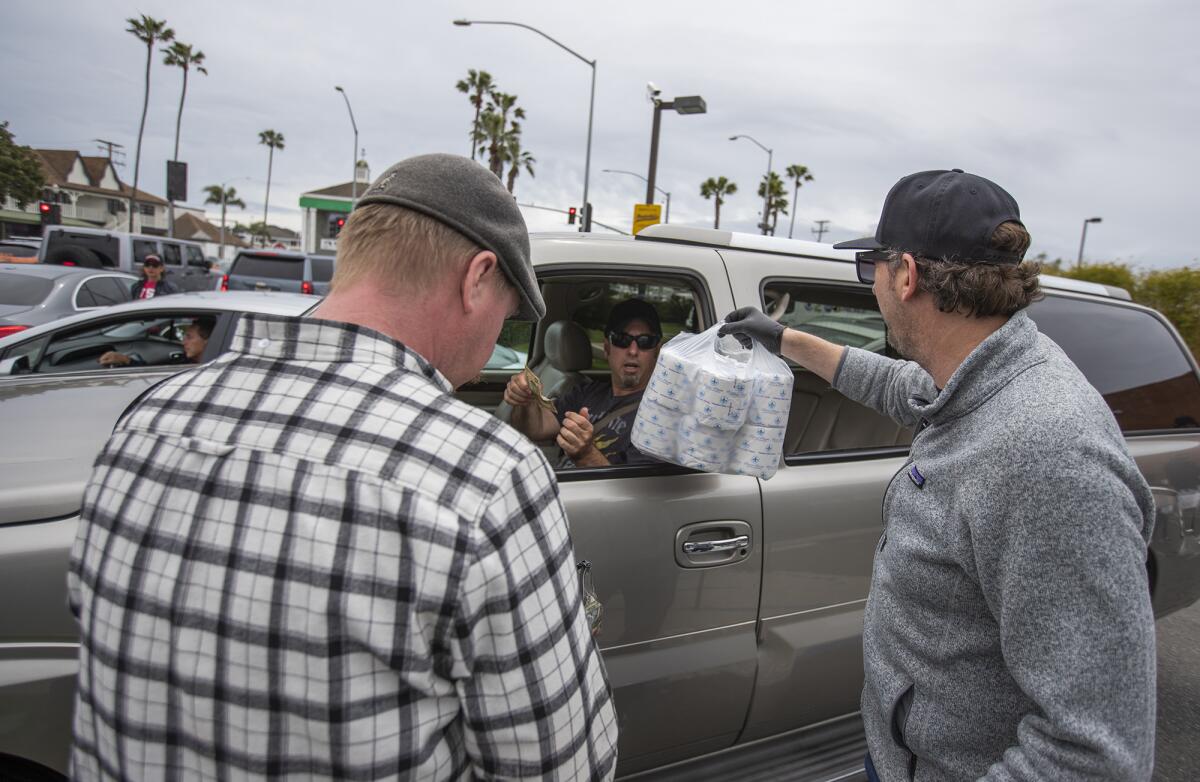 Troy Barton, left, and Malarky's Irish Pub owner Mario Marovic hand a bundle of toilet paper to a customer in the Malarky's parking lot in Newport Beach on Friday. The bar sold thousands of rolls of toilet paper at a rate of 50 cents each.