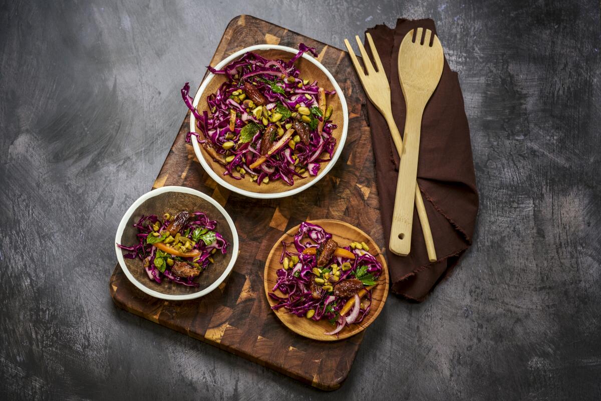 Overhead view of three plates with a slaw-like salad on a cutting board, with salad tossers next to them