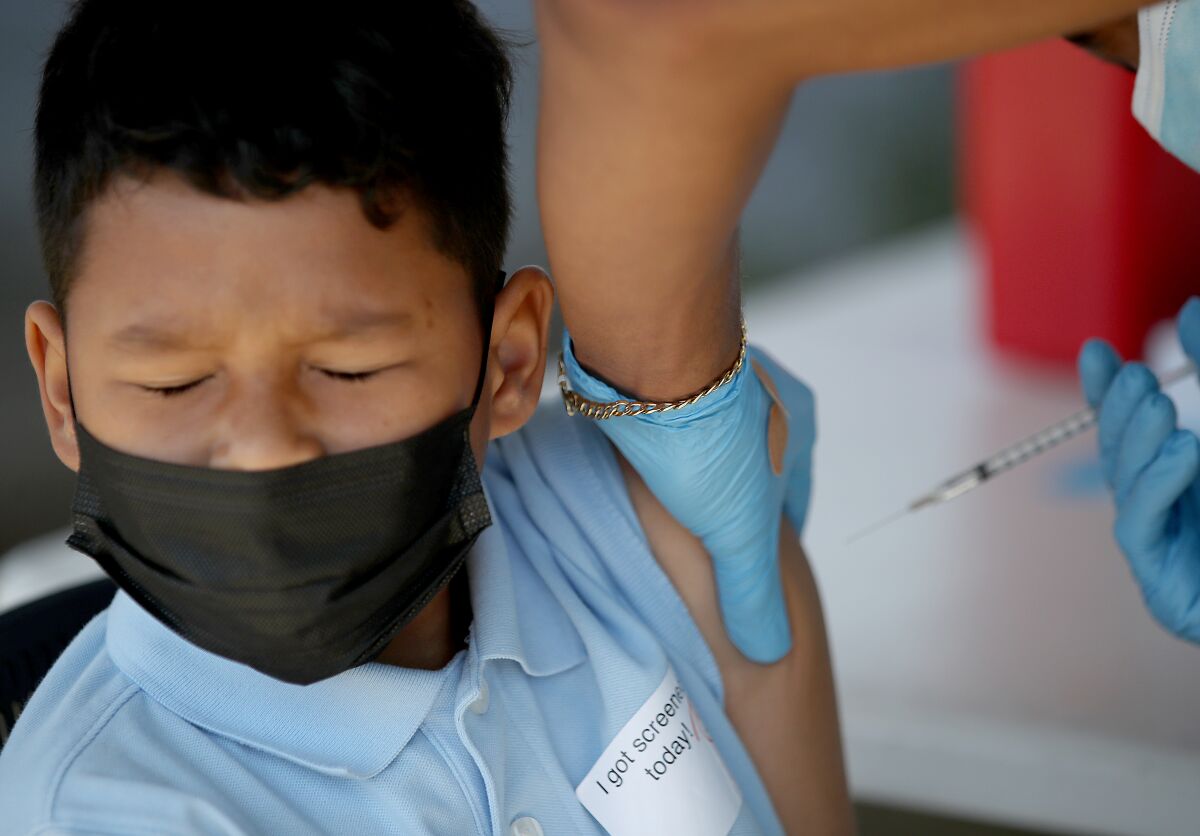 A child winces as he gets a shot of the Pfizer vaccine at school.