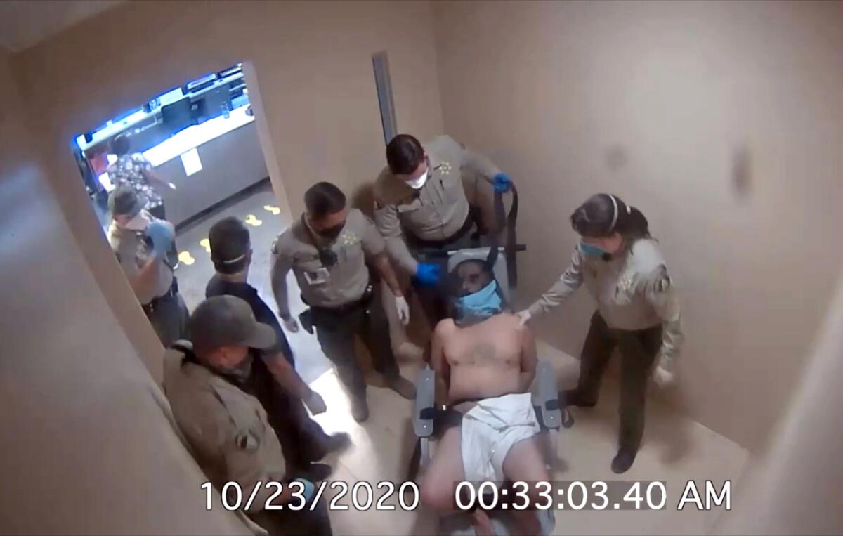 An image from security video shows a man with a towel over his lap surrounded by uniformed jailers.