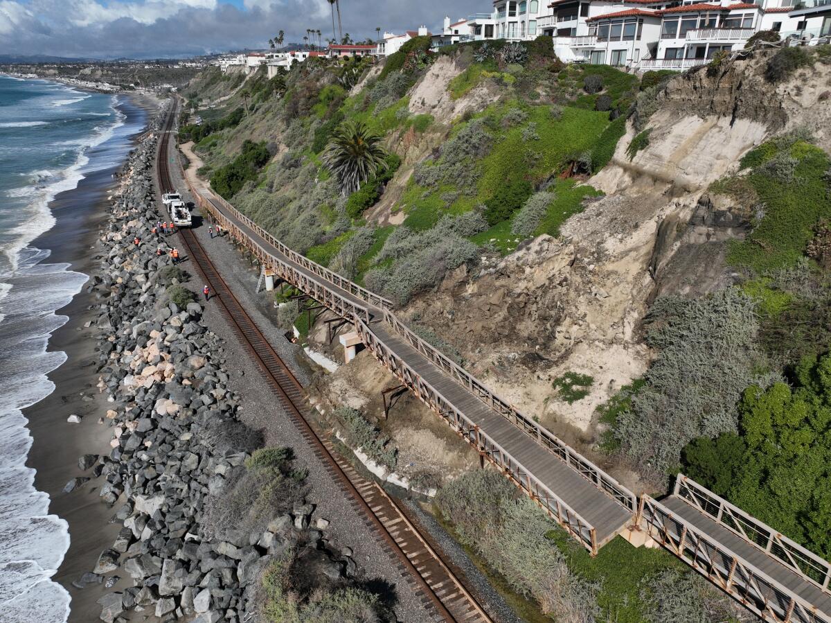 A broken walkway and railroad tracks amid a landslide in a cliff.