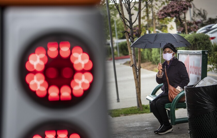 A woman holds an umbrella while sitting on a bus bench